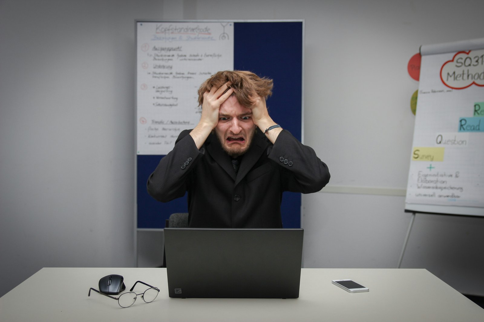 Person looking stressed while working at a laptop in front of project planning boards.