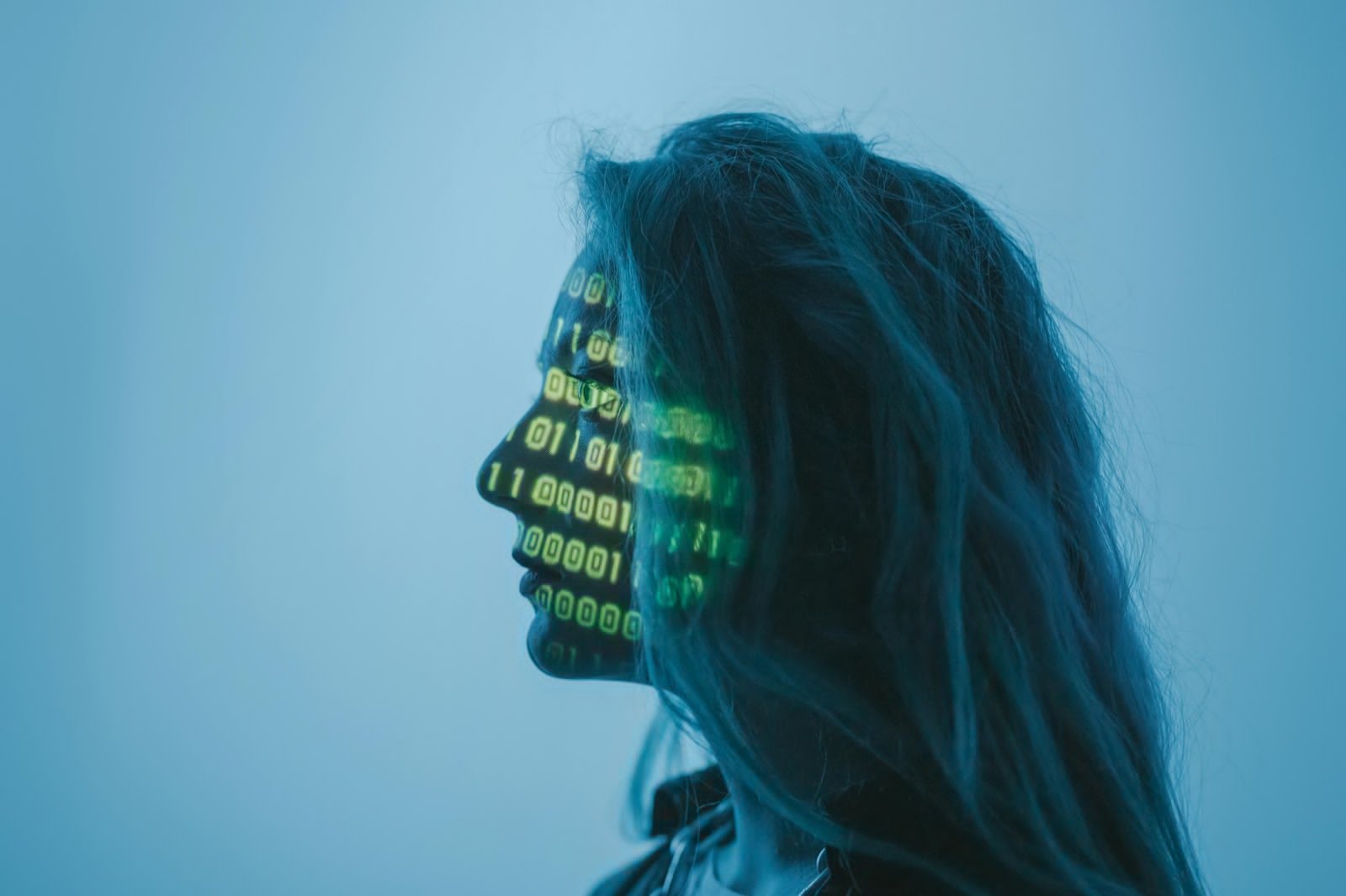 Profile portrait with binary code projected across the face in cool blue light.