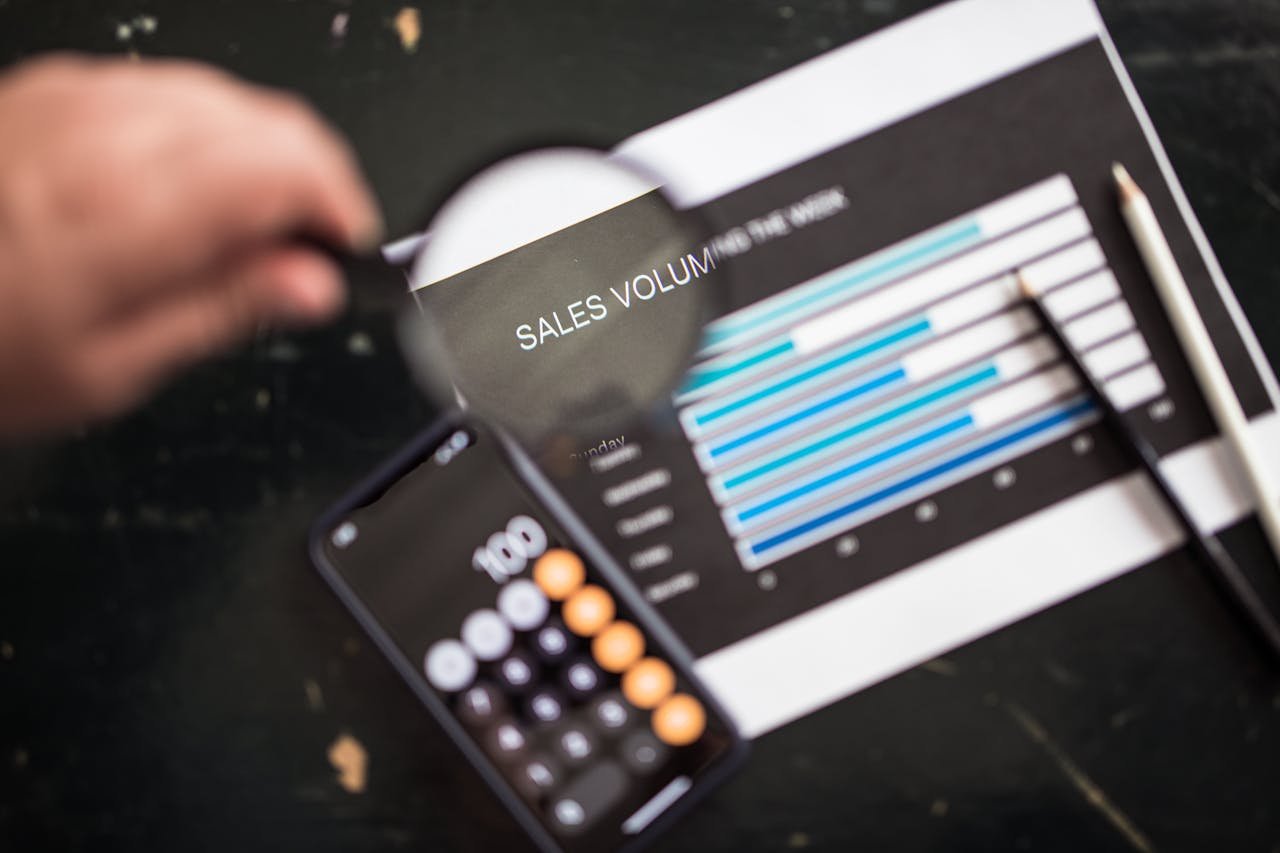 A magnifying glass over a sales chart beside a calculator and pencil, representing lead leakage analysis, response tracking, and revenue visibility.