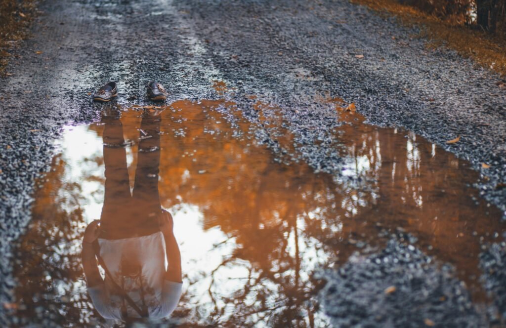 pexels-photo-2531597-2531597 Reflective image of shoes and person in muddy puddle on an unpaved road.